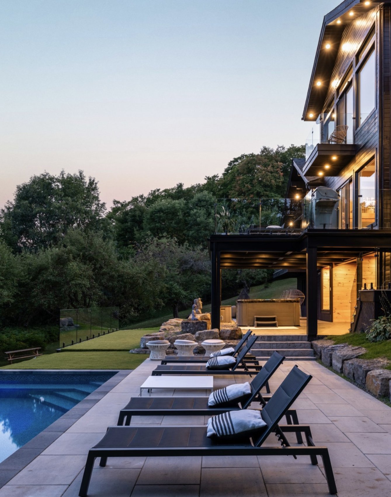 A contemporary luxury residence at dusk with an infinity pool and lounge terrace overlooking the treeline
