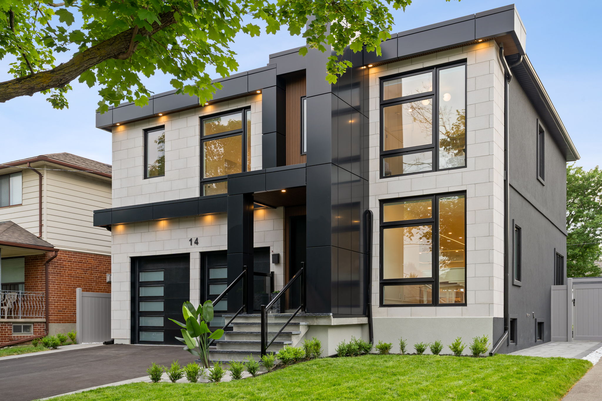 A contemporary two-story home with a white stone facade, black architectural accents, and floor-to-ceiling windows
