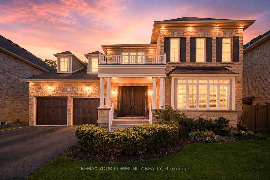 A two-story stone residential home at golden hour with warm interior light glowing through the windows